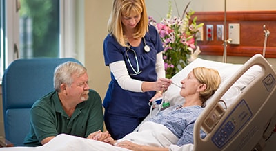 Post-Acute care staff putting thermometer in patient's mouth while the patient's husband looks on