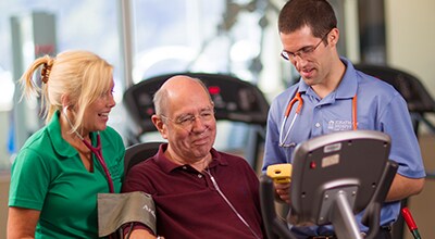 Two Cardiac Services team members discussing with patient on an exercise bike